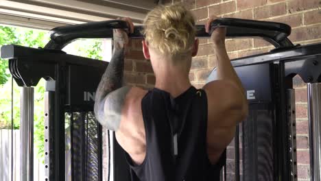 muscly man in home gym exercising chin ups from behind