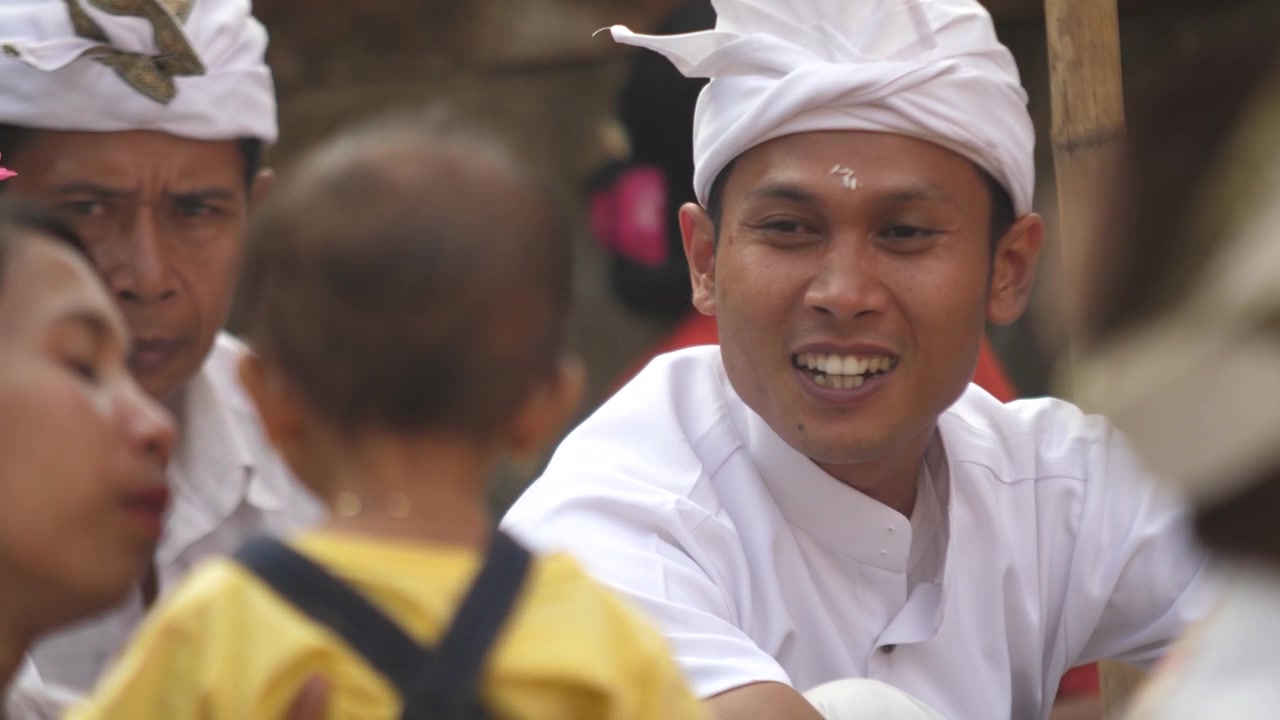 Pria Hindu dengan pakaian keagamaan tradisional berbicara dengan bayi dan membuat ekspresi lucu untuk menghiburnya sambil menunggu upacara dimulai di kuil. Pria bermain dengan gadis kecil.