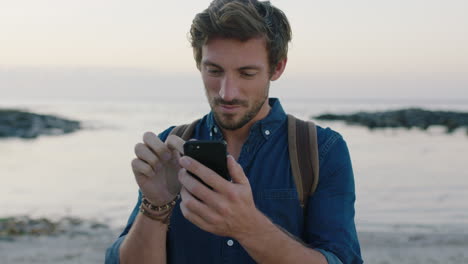 portrait of attractive caucasian man using smartphone texting on beach