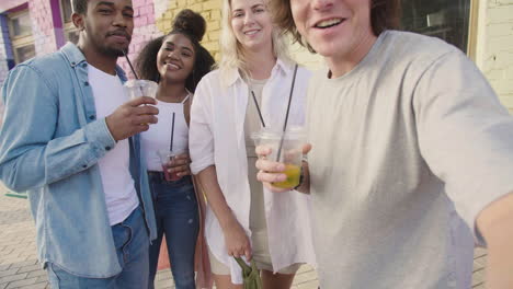 Grupo-De-Jóvenes-Amigos-Tomando-Selfies-Juntos,-Riendo-Y-Divirtiéndose-Al-Aire-Libre,-Mientras-Sostienen-Sus-Bebidas-Frescas-En-Vasos-De-Plástico