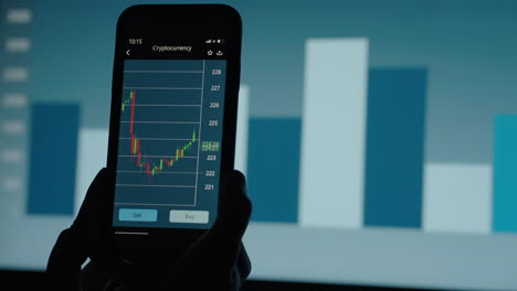 Geschäftsfrau,-Die-Auf-Dem-Smartphone-An-Der-Börse-Handelt,-Mit-Börsenfinanzbildschirm-Im-Hintergrund.-Börsen-Kryptowährungspreisdiagramm-Auf-Einem-Smartphone-Bildschirm.
