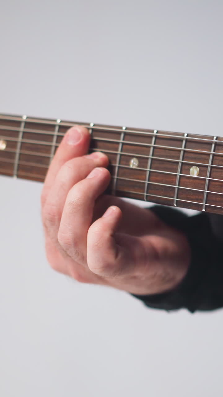 vista cercana de la mano del guitarrista tocando una guitarra roja, detalle enfocado contra un fondo blanco suavemente borroso