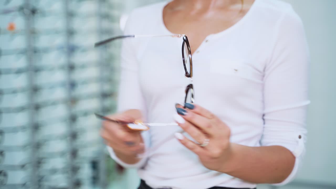 Young woman holding new eyeglasses in the optical store. Stylish glasses in black frame in the hands of a woman. Close-up.