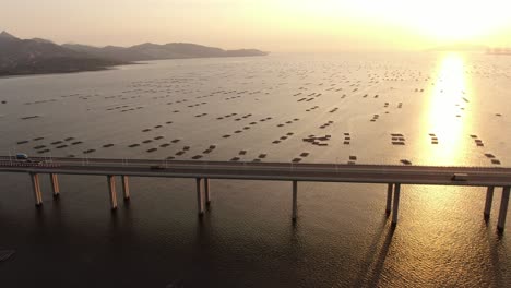 Traffic-on-Hong-Kong-Shenzhen-Bay-Bridge-at-Sunset,-with-Fish-and-Oyster-cultivation-pools,-Aerial-view