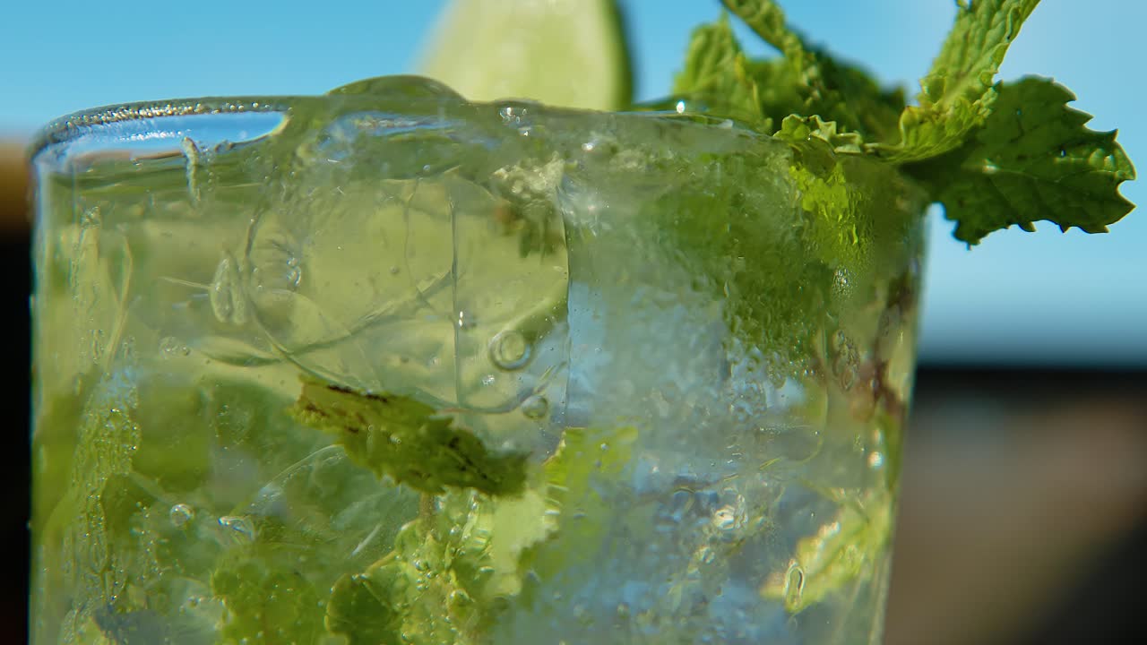 Rack focus of mint sprigs as bubbles rise in mojito, shallow depth of field