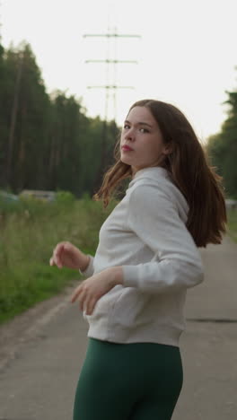 mujer corre mirando hacia atrás pasando el bosque. mujer joven con el cabello suelto corriendo por la acera en la noche cálida. rutina saludable para mejorar el bienestar general