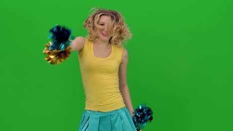 the cheerleader vigorously moves her hips, arms, whirls, does vertical splits and waves her hair. a blonde is dancing a jubilant dance in the studio on a green screen. close up. slow motion