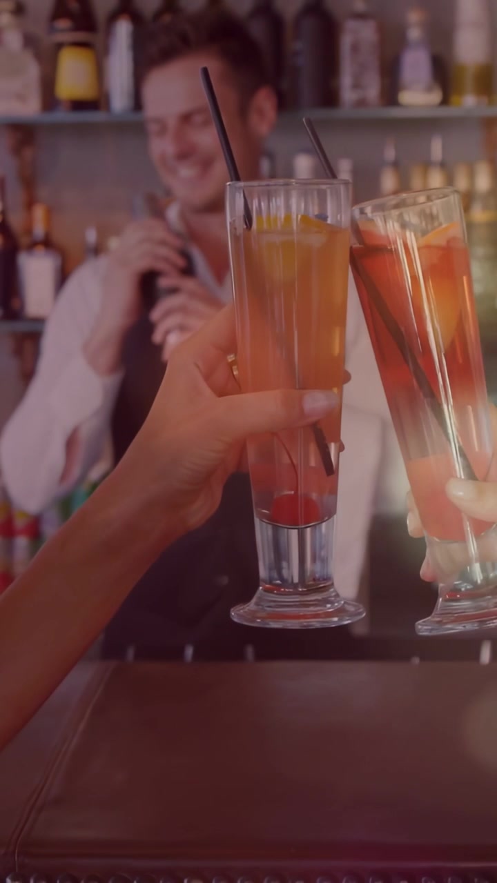 Vertical video: Bartender ending shake at bar, patrons toasting drinks, glow rising around glasses