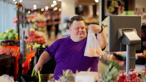 A-happy-overweight-man-in-a-purple-T-shirt-and-short-hair-puts-a-bag-of-groceries-on-special-scales-in-a-supermarket-to-get-a-price-tag-on-them-and-find-out-the-weight.-Self-weighing-food-in-the-supermarket