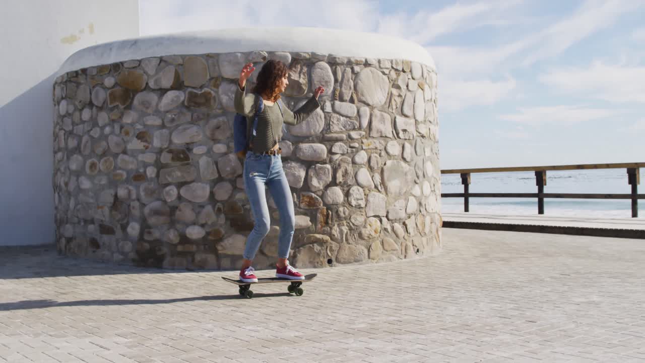 Happy mixed race woman skateboarding on sunny promenade by the sea