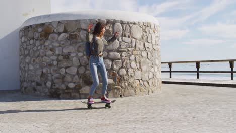 Glückliche-Gemischtrassige-Frau,-Die-Auf-Der-Sonnigen-Promenade-Am-Meer-Skateboard-Fährt