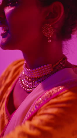 vertical video head and shoulders studio shot of female kathak dancer performing dance wearing traditional indian dress against purple background 2