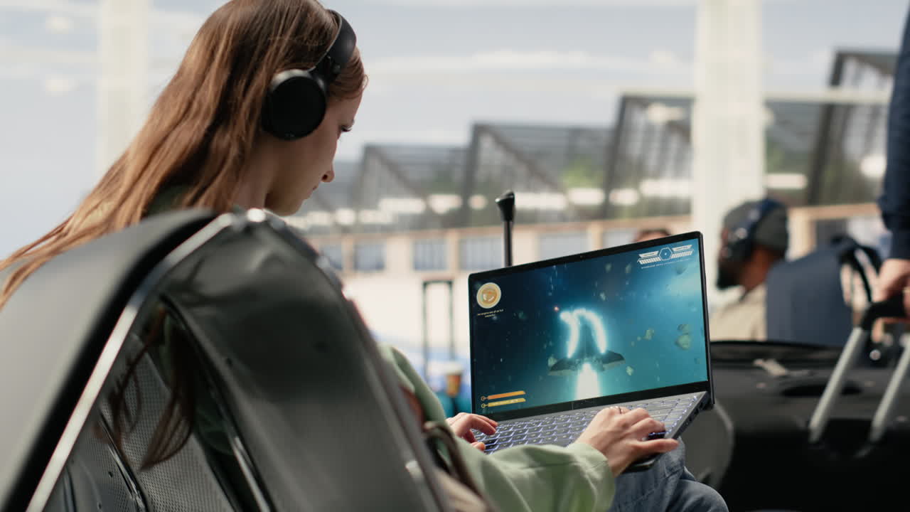 Young Woman Wearing Headphones Playing Video Game on Laptop at Airport