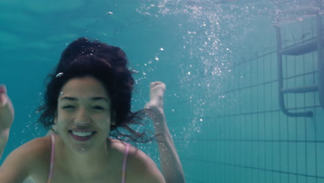 Hermosa-Mujer-Nadando-Bajo-El-Agua-En-La-Piscina-Sonriendo-Saludando-Con-La-Mano-Mujer-Atractiva-Disfrutando-Nadando-En-Agua-Clara-4k