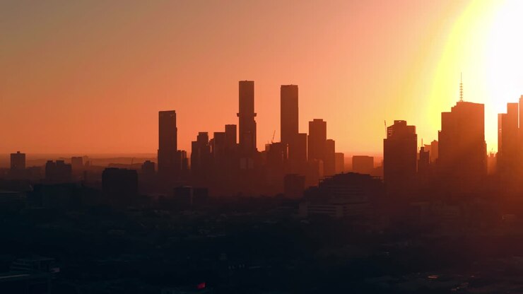 Sol dourado brilhante baixando atrás dos arranha-céus de Melbourne, luz solar intensa lançando um brilho forte sobre a vista do horizonte de Abbotsford, abordagem aérea, edifícios em camadas.