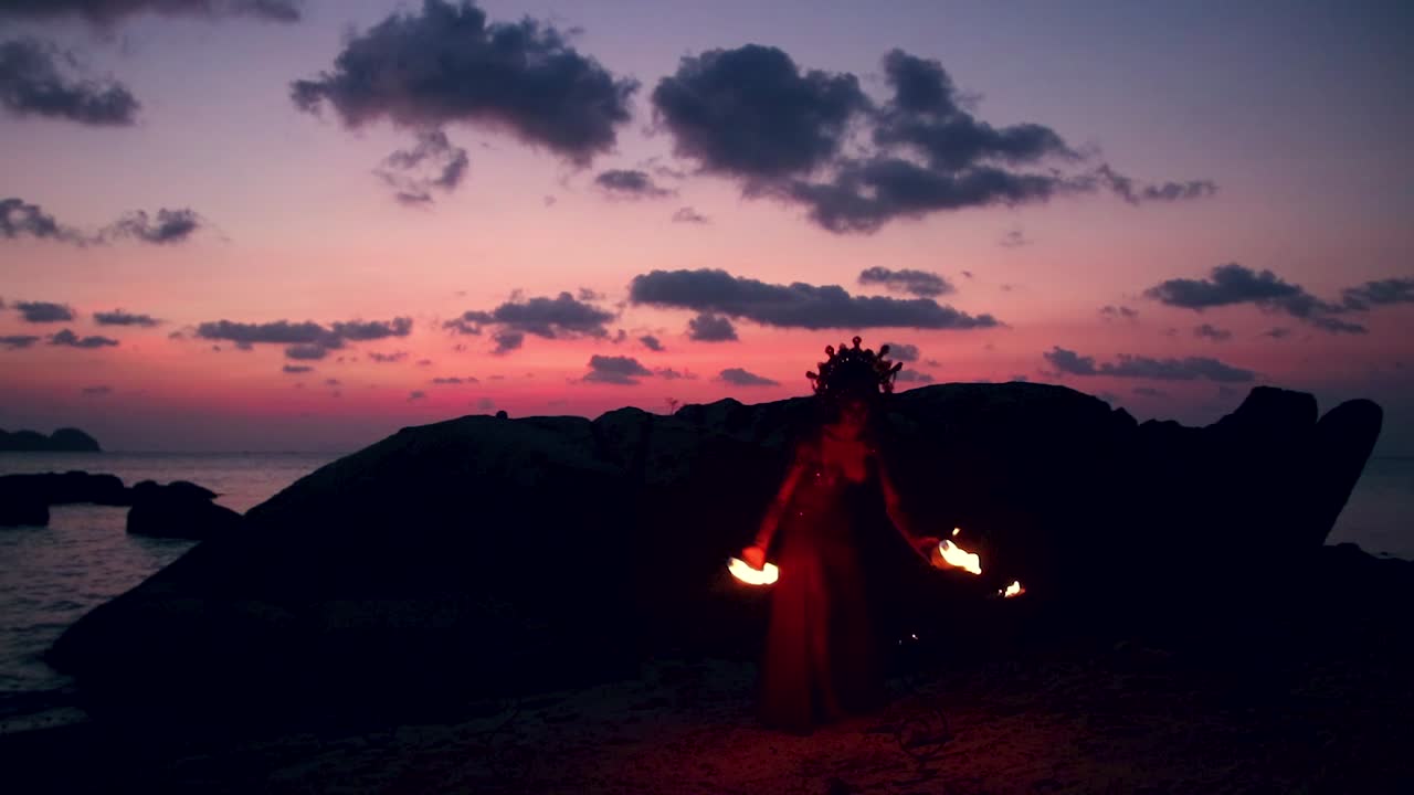 Erotic and sensual belly dancer, igniting the fire for performing with fire props on the beach during golden hour.