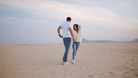 Nice-lovely-cheerful-laughing-couple-wearing-casual-white-T-shirts.-Dark-haired-guy-spinning-with-his-lady,-holding-hands-in-moves.-Dancing-on-nature-in-empty-desert.-Full-length.-Slow-motion