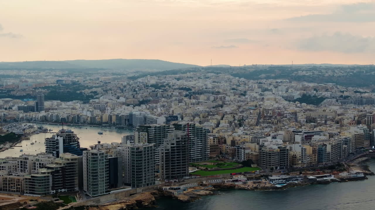 Vista aerea che gira intorno a palazzi residenziali, nuvoloso, sera d'estate a Malta