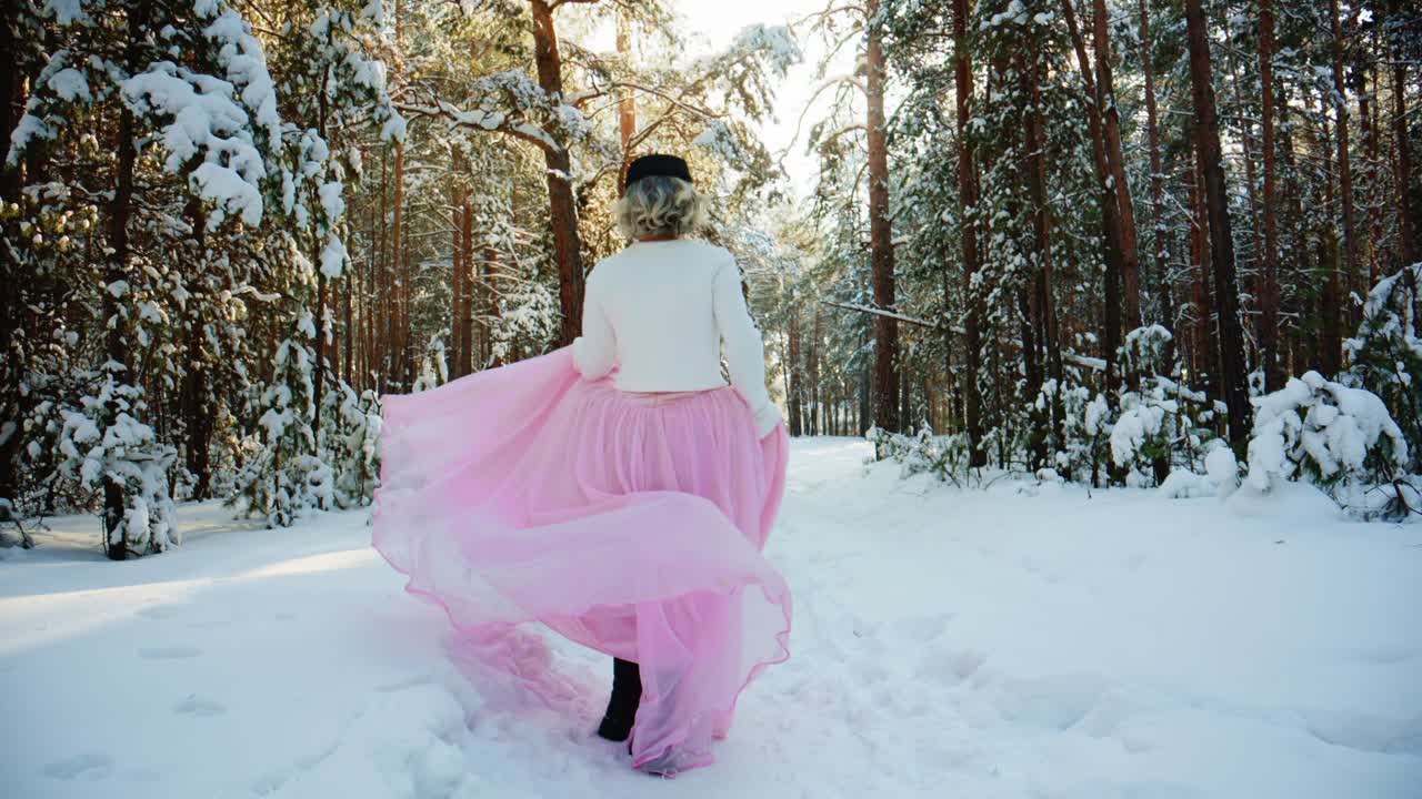 Donna elegante in gonna rosa che cammina attraverso una magica foresta innevata