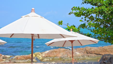 sombrillas de playa blanca y mar tropical azul en la brisa de verano, detalle