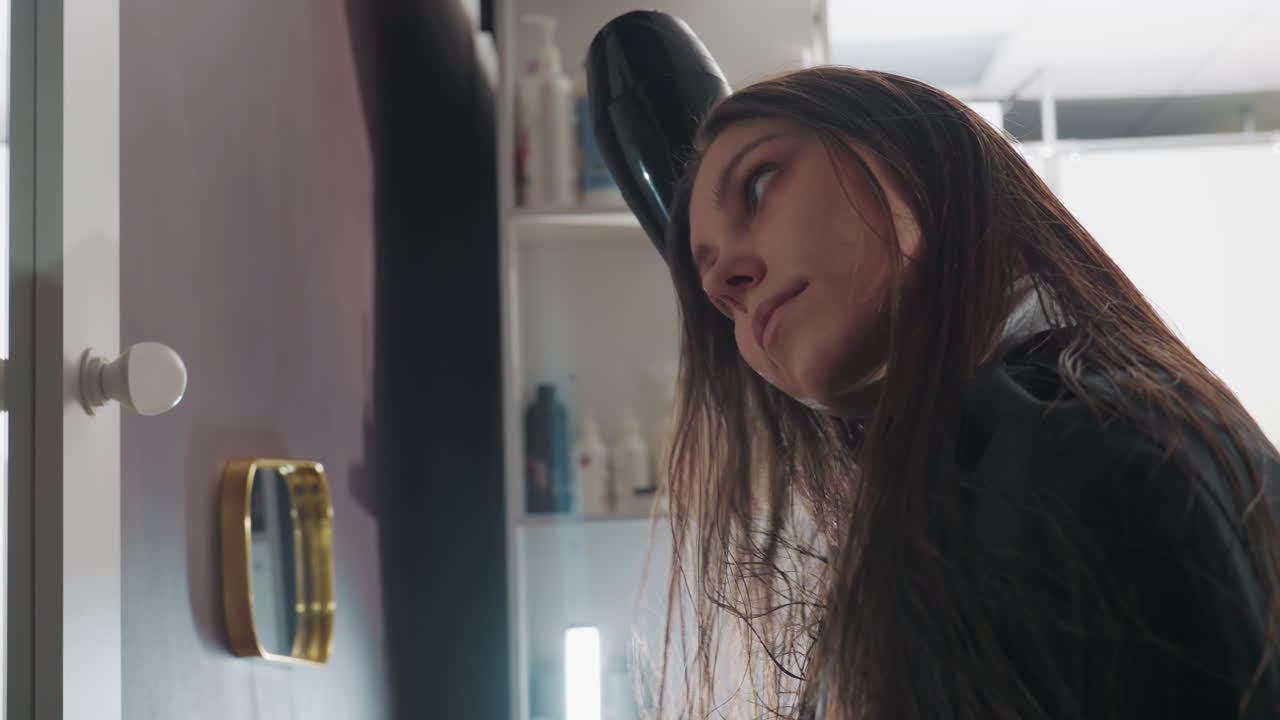 secado de pelo elegante, escena serena en un salón con una mujer, sesión de peinado relajada capturada en condiciones de iluminación suave, momento tranquilo de una señora peinándose en un ambiente de salón con luz tenue