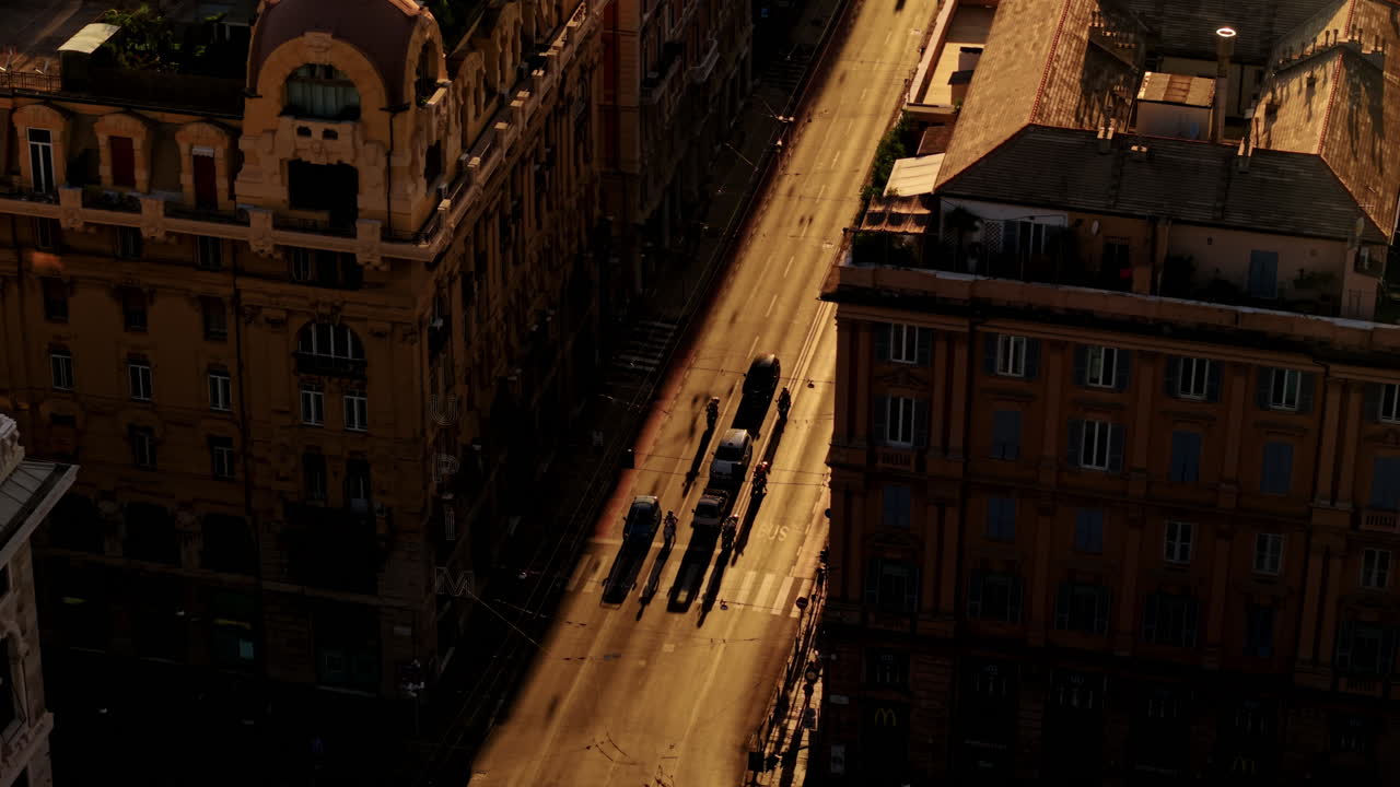 Low drone flight between buildings revealing a sunlit street in Genoa with vehicles and long shadows at sunset