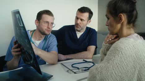 two male caucasian doctors discussing over medical x-ray scan with a female patient