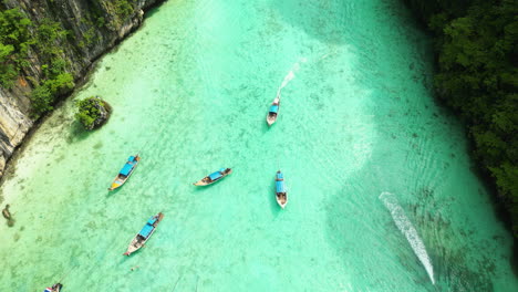 crystal clear turquoise waters and limestone cliffs at maya bay in phi phi islands, longtail boats at maya bay, thailand, aerial view