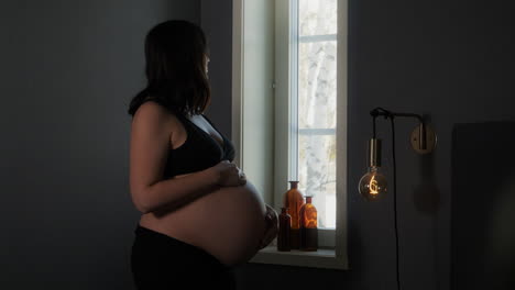 Heavily-pregnant-woman-touches-bump-and-gazes-out-window