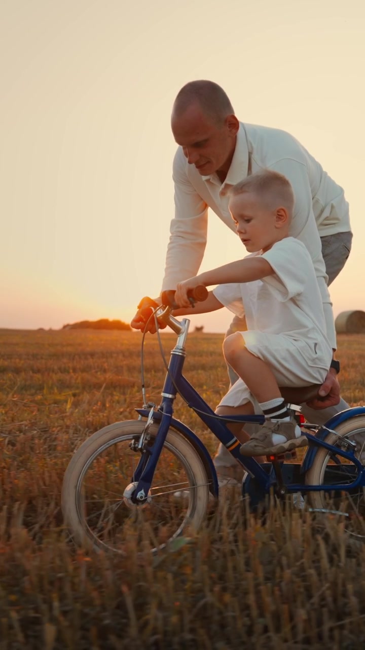 Padre che insegna al figlio piccolo ad andare in bicicletta in un campo al tramonto