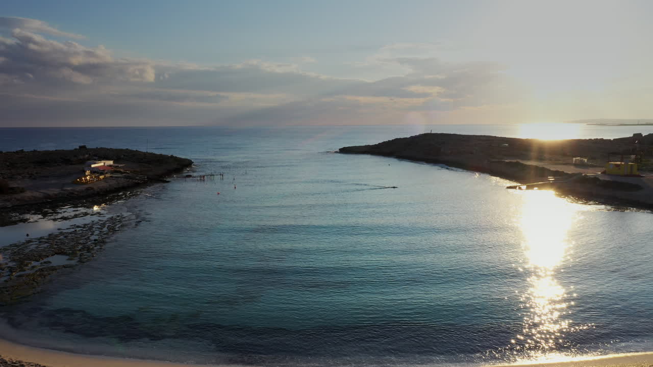 toma aérea de una pequeña playa de arena, volando sobre un solo nadador durante la hora mágica