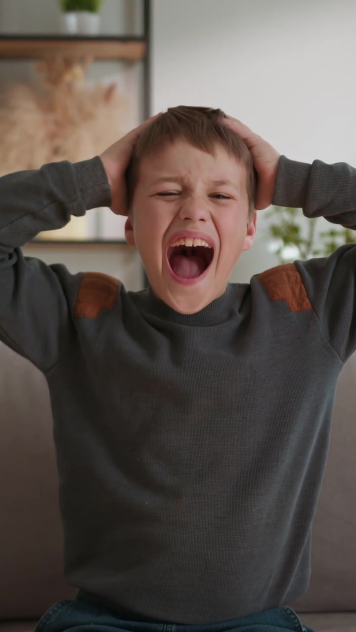 Young boy expresses extreme distress and frustration by screaming with hands on head indoors