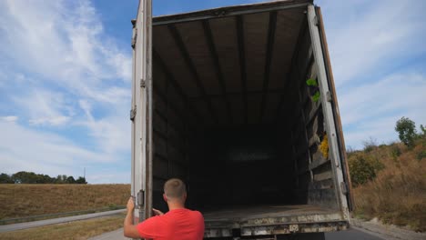 male driver opening rear door of truck at countryside. lorry parked at country road. car is ready for loading the goods. beautiful landscape at background. logistics concept. close up slow motion