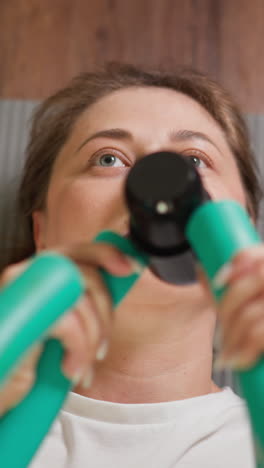 mujer dobla el expansor de mariposa en el piso de primer plano. mujer fuerte trabaja sobre los músculos de los brazos acostada en el tapete en el gimnasio en casa. equipo de desarrollo de manos