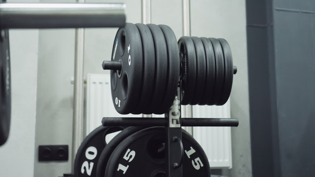 stacked black weight plates on rack with numeric labels ten fifteen twenty near radiator and cable tower in modern grey gym interior organized free weight station ready for training use