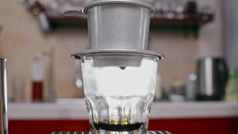 coffee dripping from a stainless steel vietnamese coffee filter into a glass cup at a coffee shop