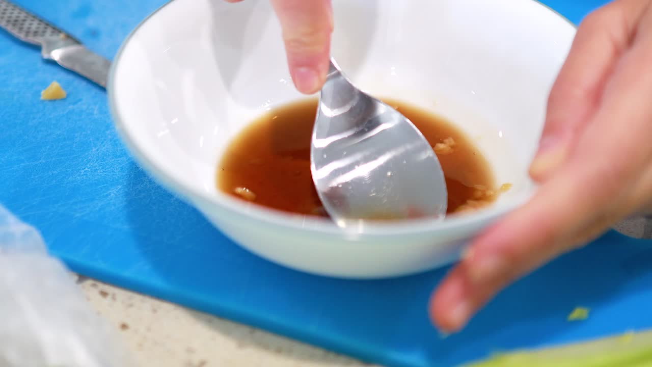 Hands dissolve palm sugar in fish sauce using a spoon. Bright kitchen setting with a focus on culinary preparation