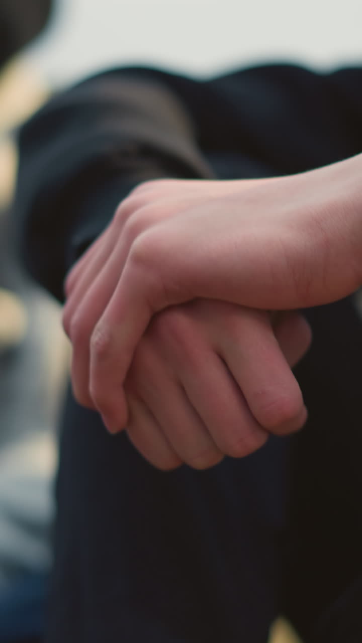 primer plano de las manos juntas mientras la persona las mueve suavemente, con un fondo borroso que muestra a otro individuo con una camiseta gris