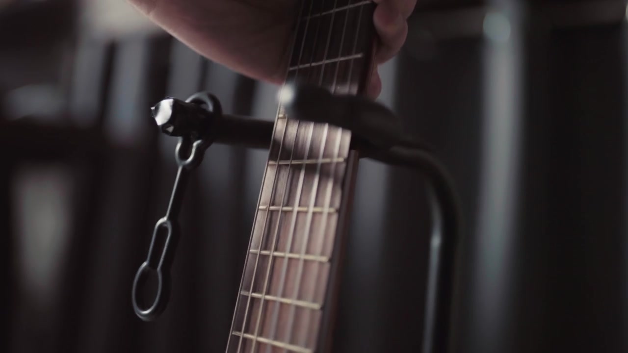 Primo piano di una mano che posiziona una chitarra su un supporto in un ambiente interno in penombra.
