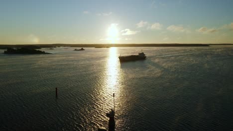 Aerial-drone-view-of-a-general-cargo-vessel-silhouette-making-way-ahead-during-morning-sunlight-in-finnish-archipelago