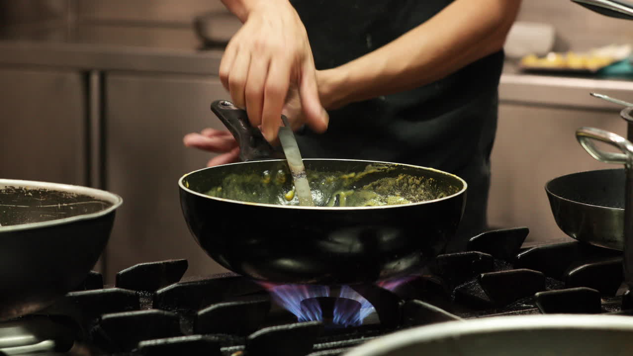 chef rociando sal en una salsa espesa y luego revolviéndola a fuego medio en una estufa de gas en la cocina de un restaurante