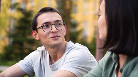 young japanese man talking and laughing with his female friend while sitting together outdoors