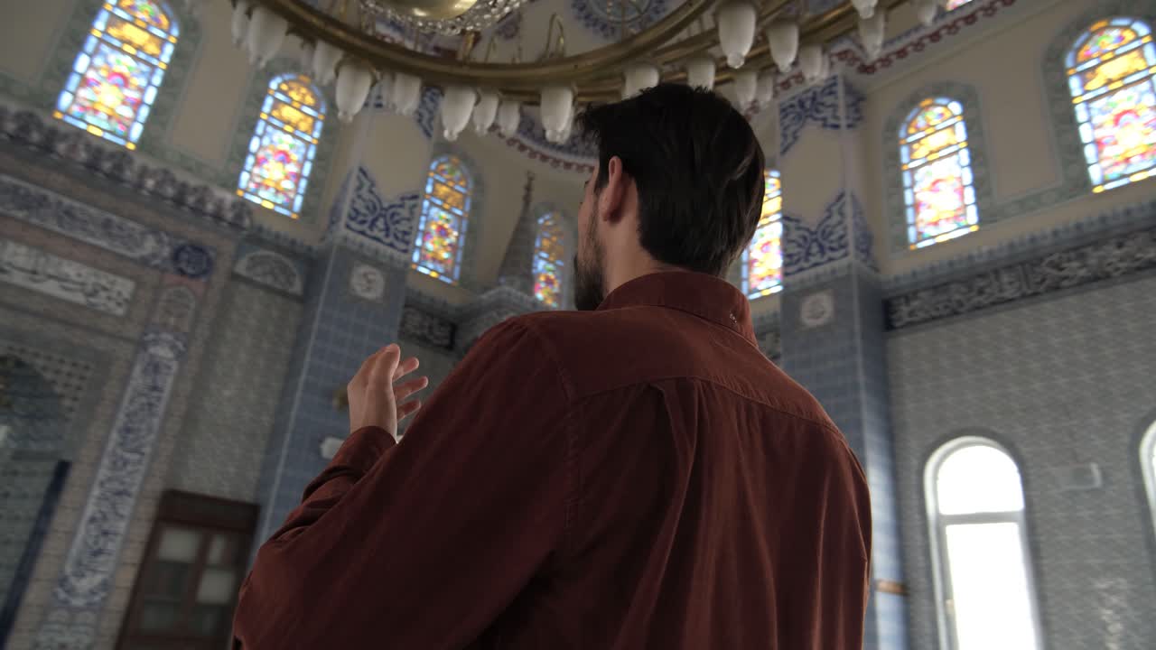 Standing young bearded man praying with open hands, Muslims who go to historical and holy places pray