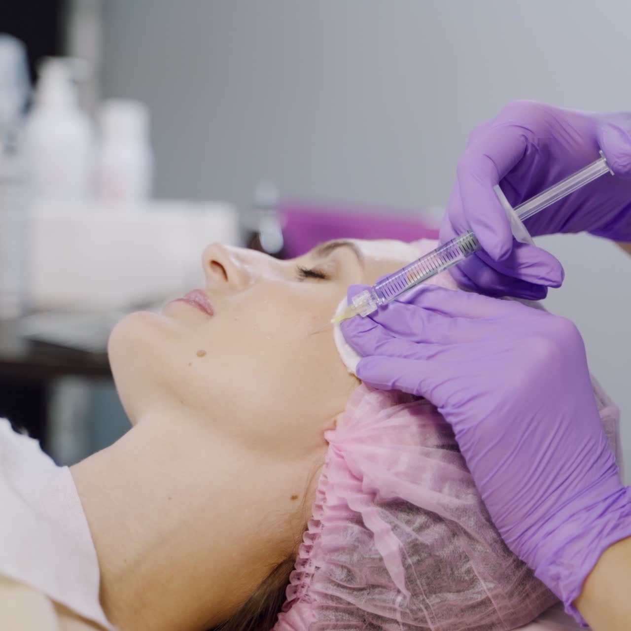 A client is undergoing mesotherapy in the beauty salon using injections on the background of different cosmetics. Beauty industry.