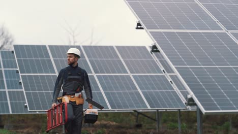 a young technician in work uniform inspects the solar power plant while walking with the necessary equipment