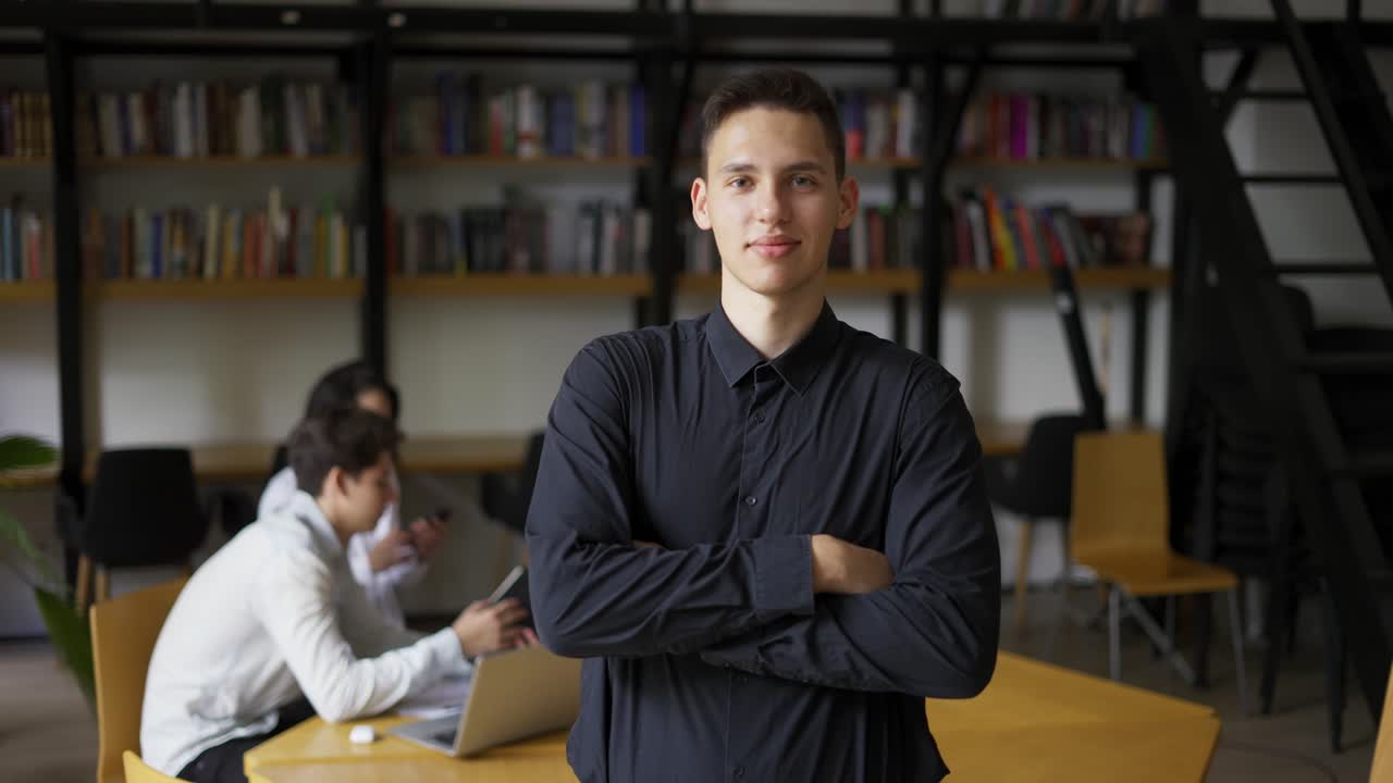 retrato de un bibliotecario caucásico mirando a la cámara seriamente cruzando las manos sobre el pecho en las estanterías de libros de fondo
