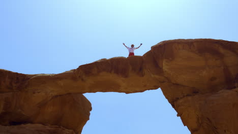 person standing on a natural rock arch in the desert