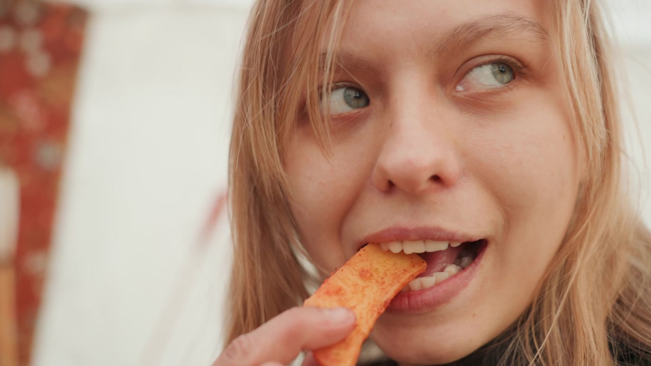 Rustikaler Food-Moment auf dem Tisch zeigt eine Keramikschale mit gewürzten Kartoffelspalten, eine Hand greift danach, eine Person beißt in eine knusprige Spalte und lächelt dann mit zufriedenem Ausdruck in warmem natürlichem Licht