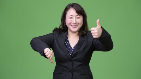 성숙하고 혼란스러운 아시아 사업가 여성은 엄지손가락을 위로하고 엄지 손가락을 아래로합니다.