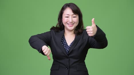 mature confused asian businesswoman giving thumbs up and thumbs down